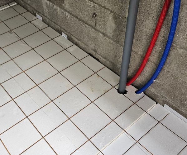 Pose de carrelage au sol avec passage de tuyaux pour la plomberie d’une cuisine d’été.